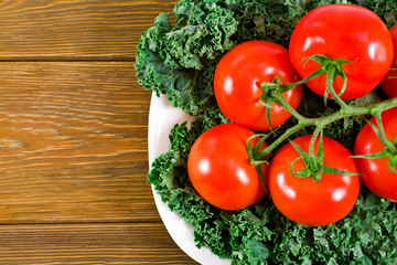 Tomatoes and a fresh leaf of kale cabbage in a white plate on a wooden background. Top view.