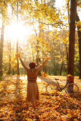 Stylish woman with a bicycle enjoying autumn weather in the park. Beautiful Woman walking  in the autumn forest.