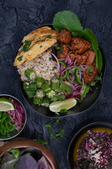 Vegan asian bowl with seitan, okra, chickpea flour omelette, pickles over brown rice and quinoa on dark background, copy space