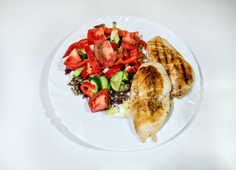 Grilled chicken breast and fresh vegetable salad on a white plate. Top view. Fitness food concept.