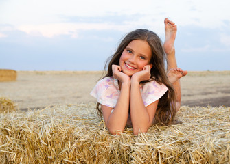 Adorable happy smiling ittle girl child lying on a hay rolls in a wheat field - 370998406
