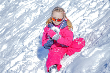 Fototapeta na wymiar Young Girl Sitting On The Snow Mountain and playing with snow ball. Winter time