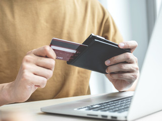 Businessman hand hold credit card to online shopping on laptop computer from home, payment e-commerce, internet banking, spending money