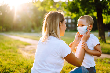 Obraz premium Mother puts on her baby sterile medical mask in quarantine city at sunset. Covid-2019.