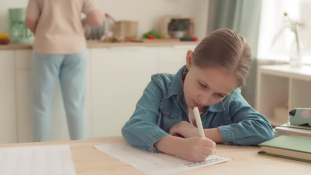Medium shot of unrecognizable woman is standing in the kitchen, cooking then checking her daughter math test, scolding her and crossing task out. Girl is upset