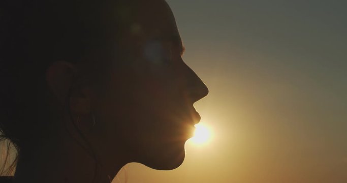 Close up female face profile silhouetted on evening sky setting sun slow motion. Happy woman kissing sun on nature background outdoors copy space text. Summer skin care products concept