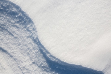 Beautiful winter background with snowy ground. Natural snow texture. Wind sculpted patterns on snow surface. Closeup top view with copy space.