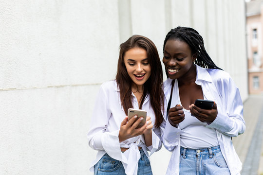 Two mixed race women friends sharing social media in a smart phone outdoors in a park