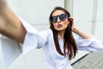 Young girl take selfie from hands with phone on summer city street. Urban life concept.