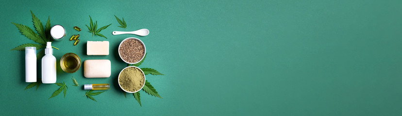 Naklejka na ściany i meble Flat lay with hemp extract products - cosmetics, lotion, face cream, body butter, soap bars, cannabis leaves, seeds, hemp oi, capsules, protein powder, flour on green background. Top view. Banner
