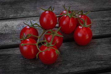 Fresh red cherry tomatoes on a brunch lying on a wooden old background. Closeup photo of organic vegetables and healthy food
