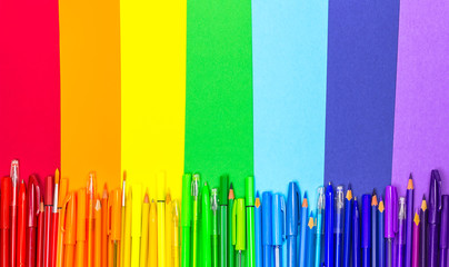 Back to school. School supplies are laid out in the form of a rainbow. Pens, pencils, markers of rainbow colors are on colored paper. The view from the top, place for text