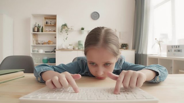 Lockdown of tied Caucasian schoolgirl is sitting at kitchen table and typing on computer keyboard