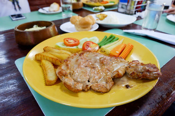 Pork steak with vegetables in yellow plate.
