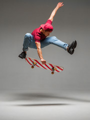 Cool young guy skateboarder jumps on skateboard in studio on grey background. Photography about skateboarding tricks - obrazy, fototapety, plakaty