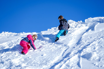 Fototapeta na wymiar Two joyful kids playing on the snowing mountain on a winter day.