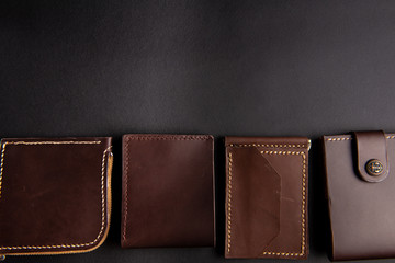 beautiful background wallets made of genuine leather of brown color made by hands are laid out on a black table. view from above. With space for an inscription. Leather craft concept.