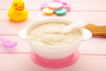 Bowl with baby food with toys on pink background