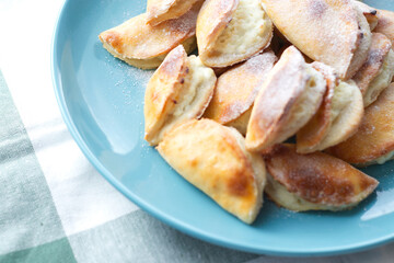 homemade cakes, cottage cheese pies in powdered sugar, on a blue plate, on a white towel with a green strip. pastries for tea, warm welcome, cooking at home. Fast weight gain, carbohydrates, sweets