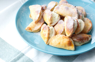 homemade cakes, cottage cheese pies in powdered sugar, on a blue plate, on a white towel with a green strip. pastries for tea, warm welcome, cooking at home. Fast weight gain, carbohydrates, sweets