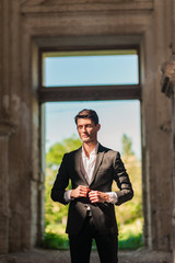Male Handsome groom waiting for the bride on the background of beautiful architecture. Rich groom on the wedding day. Elegant groom in a black suit . Wedding day