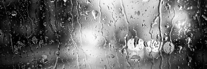 Panoramic image. Blurred car lights in black and white. Raindrops on the front window