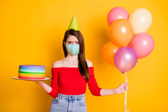 No guest anniversary party. Upset girl in medical mask celebrate birthday hold balloons cake frustrated wear red casual top denim jeans cone isolated over bright shine color background