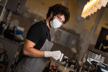 Young man, barista, making coffee espresso while wearing surgical mask and gloves for preventing corona virus spread - Bar safety working concept.
