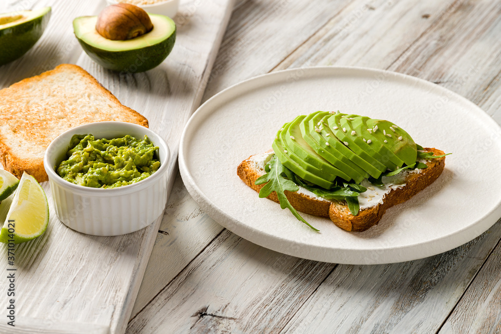 Wall mural Toast with avocado, cream cheese,guacamole and arugula on white wooden table - Wall murals