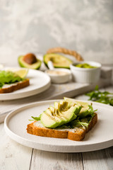 Toast with avocado, cream cheese,guacamole and arugula on white wooden table