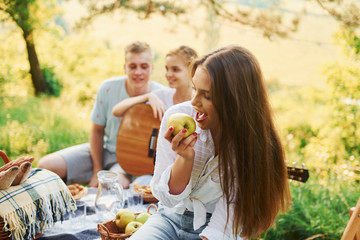 Obraz premium Woman eats apple. Group of young people have vacation outdoors in the forest. Conception of weekend and friendship