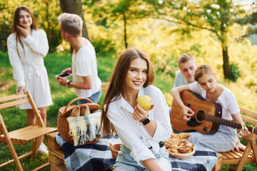 Woman eats apple. Group of young people have vacation outdoors in the forest. Conception of weekend and friendship