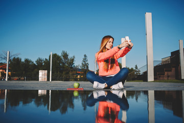 Gorgeous young woman making self portrait while holding up her smart phone, beautiful hipster girl take pictures of her self with cell phone, female teenager having fun in the park