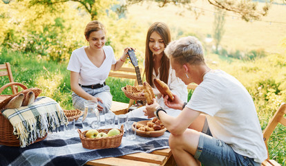 Sitting by picnic table. Group of young people have vacation outdoors in the forest. Conception of weekend and friendship