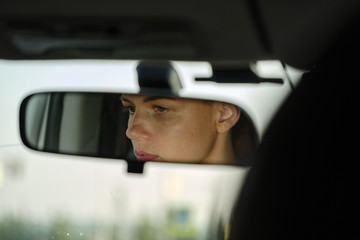 Reflection of young female face and eyes in rearview mirror of a car. Woman driver. Selective focus 