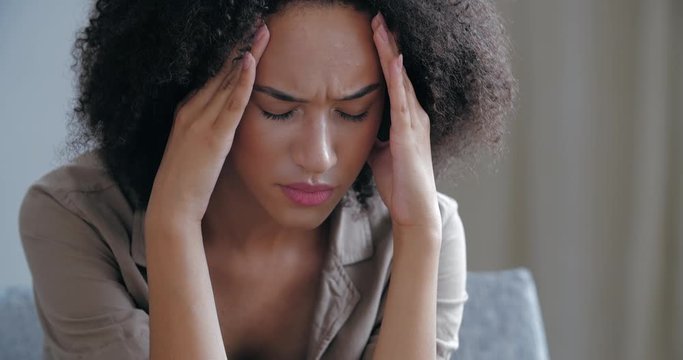 Curly upset worried girl feels stress and upset, cannot solve bad situation. Young afro american woman suffering from headache weak sensation soreness, lady holding her forehead with hands in grief