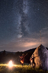 Romantic couple having a rest in the mountains, a girl dancing next to the fire and a guy playing...