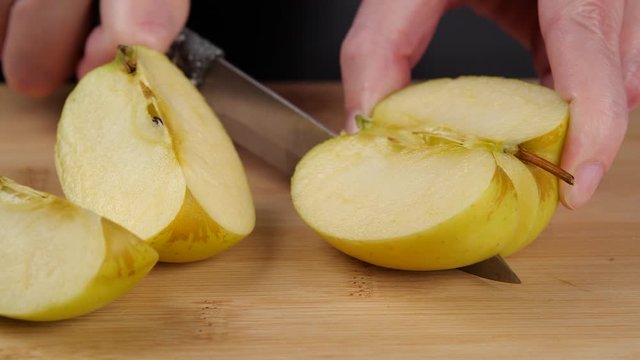 Closeup unrecognizable person dividing fresh ripe apple on pieces with knife on cutting board