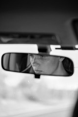 Reflection of young female face and eyes in rearview mirror of a car. Woman driver. Selective focus. Black and white.