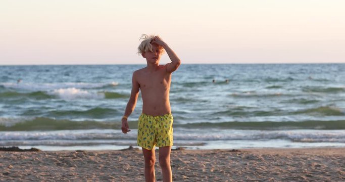 Young handsome blond teen boy with blond hair and forelock in yellow swim shorts flipping on the sand beach. Copy space. 