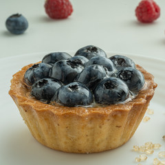 Blueberry tartlets served on a white plate with brown sugar. Glass of milk in the sun on a white background.