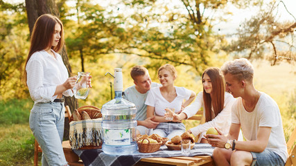 Big plastic water bottle on table. Group of young people have vacation outdoors in the forest. Conception of weekend and friendship
