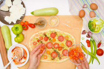 step by step recipe for cooking homemade vegan pizza with zucchini, tomatoes, peppers, mozzarella . hands of a woman preparing a pizza from the top view . light background
