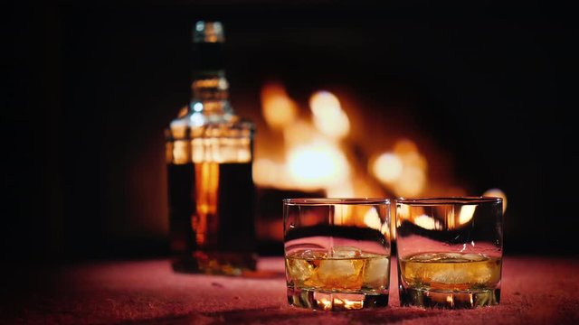 Strong alcohol in two glasses and a bottle, in the background a fire burns in the fireplace