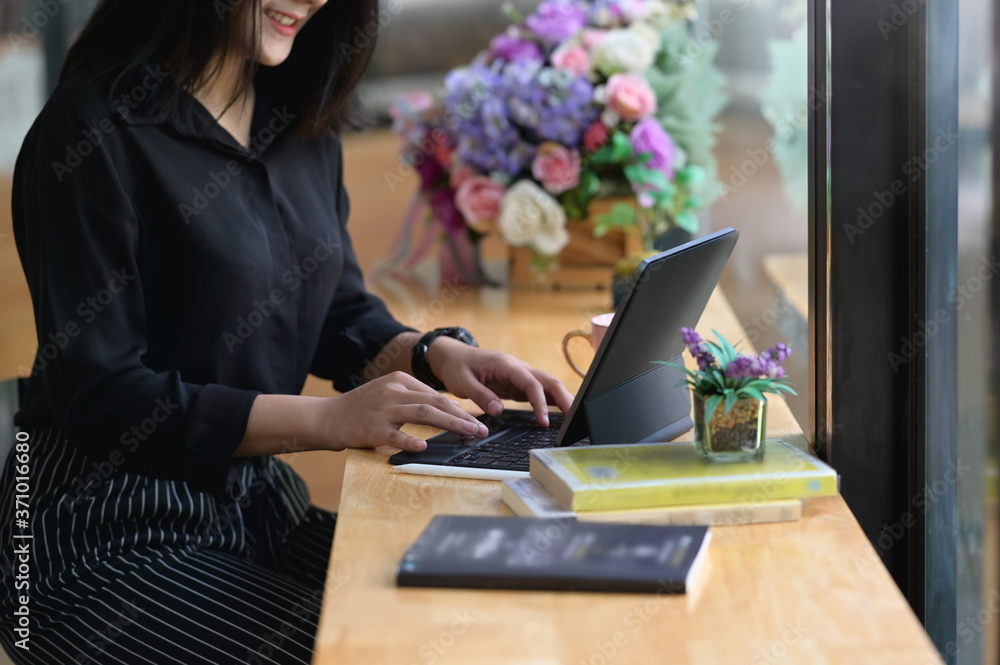 Poster a woman is using a computer tablet while sitting at the wooden counter.