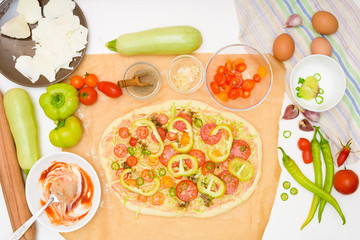 step by step recipe for cooking homemade vegan pizza with zucchini, tomatoes, peppers, mozzarella . hands of a woman preparing a pizza from the top view . light background