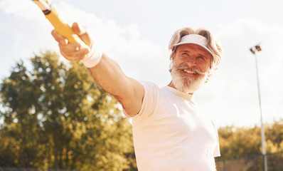 Beautiful sunlight. Senior stylish man in white shirt and black sportive shorts on tennis court