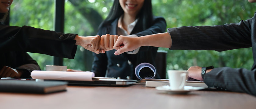 Businesspeople are greeting each other with hand bumping while sitting at the meeting table.