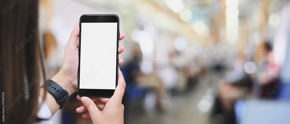 Poster cropped image of hands is using a white blank screen smartphone in public train.