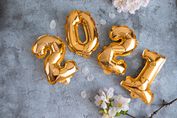 Gold 2021 balloons numbers and apple tree branches on a concrete background
